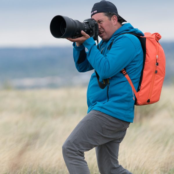 f-stop Ambassador David Clifford wearing the f-stop Dalston Urban Series 21 liter camera backpack in the Nasturtium color option and holding a Nikon D5 DSLR and a Nikon 200mm lens
