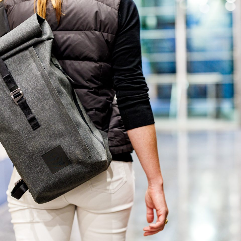 f-stop Dyota 11 liter sling camera bag in the Battleship Grey color option being worn by a female model in an urban/office environment