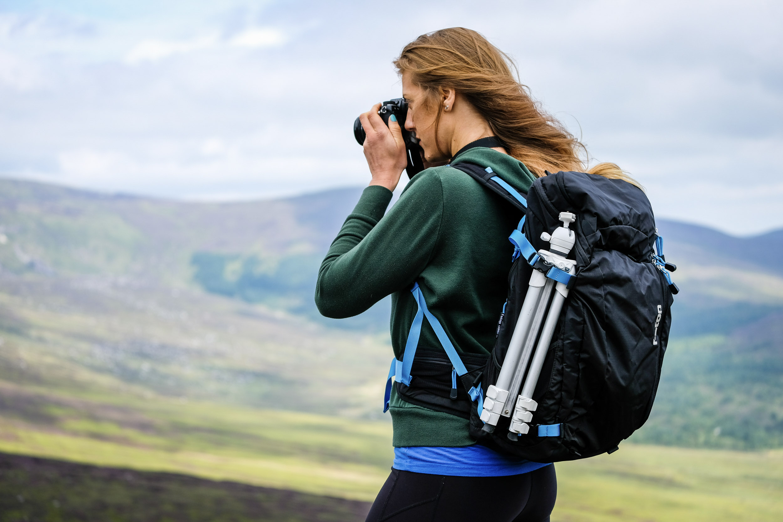 f-stop Ultra Light Series worn by a woman holding a camera with mountains in the background