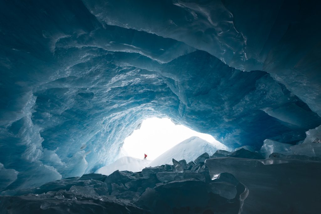 f-stop Ambassador Monika Deviat pictured from a distance through an Ice Cave while wearing the f-stop Tilopa 50 liter camera backpack in Magma Red color option