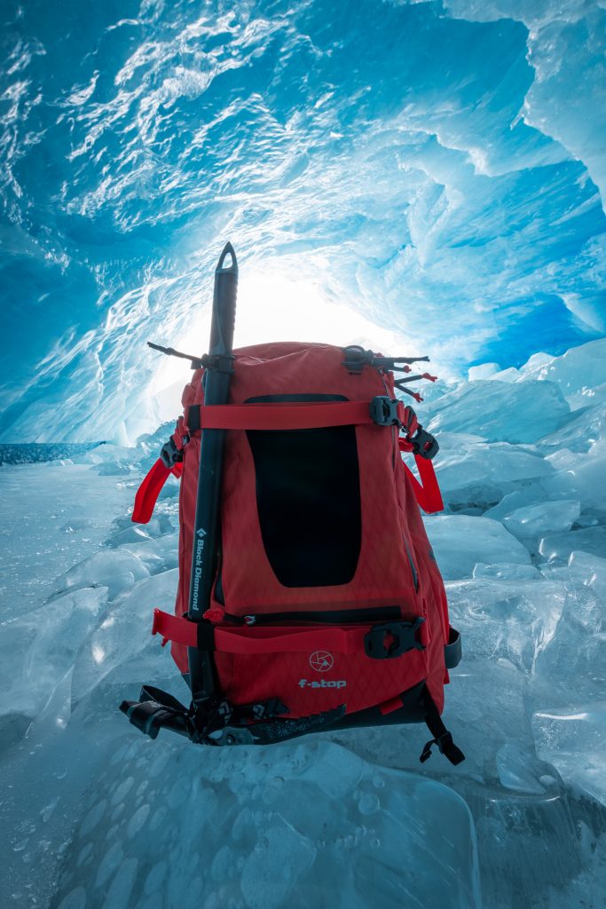 A picture of the f-stop Tilopa 50 liter camera backpack in Magma Red color option pictured in an ice cave taken by by f-stop Ambassador and Astrophotography specialist Monika Deviat