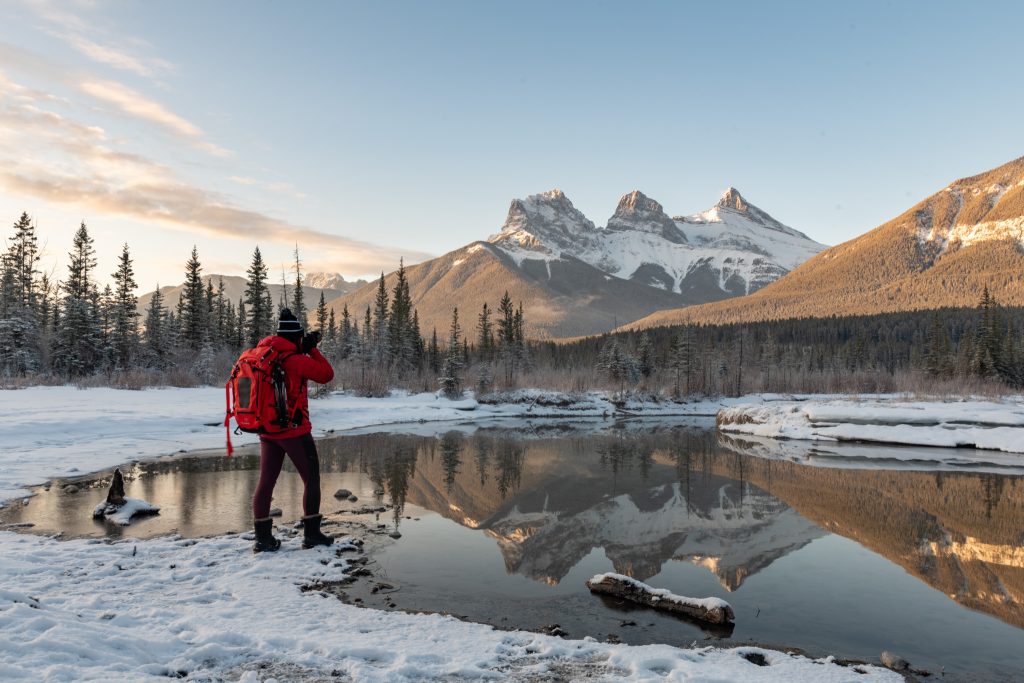 f-stop Ambassador Monika Deviat pictured photographing in a mountain landscape with a reflection in the lake while wearing the f-stop Tilopa 50 liter camera backpack in Magma Red color option. Photographed by f-stop Ambassador and Astrophotography specialist Monika Deviat