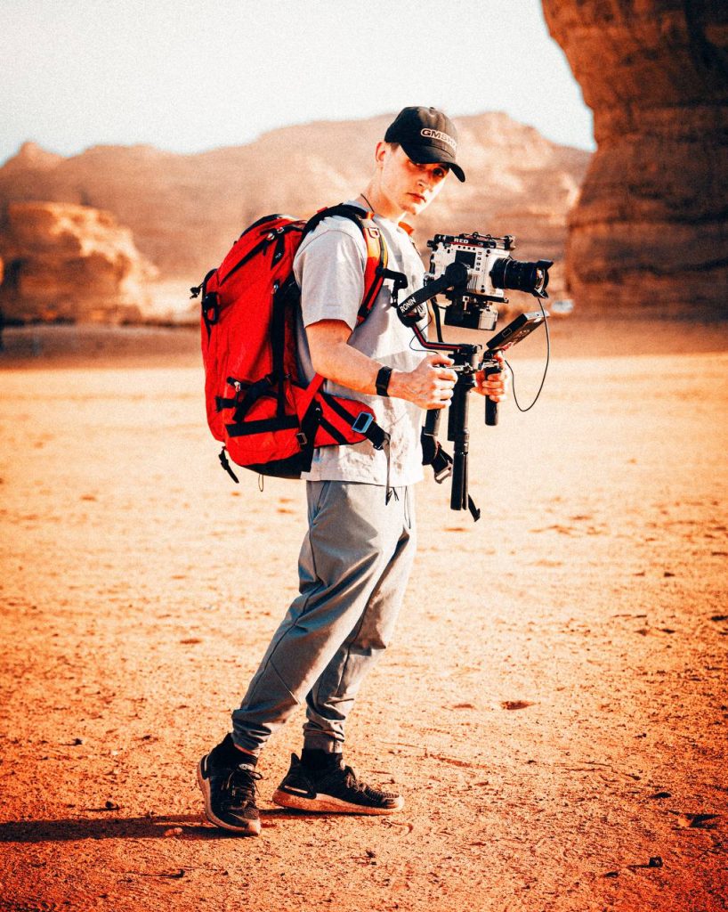 f-stop Ambassador Nick Leavesley with his Tilopa 50 liter Duradiamond® camera backpack in the Magma Red color option and carrying his RED V-Raptor camera system